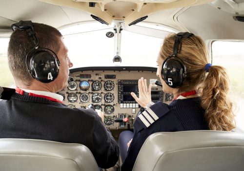 Rear view of pilot trainee and female flight instructor in cockpit. He is sitting next to the female instructor attending to her explanations.